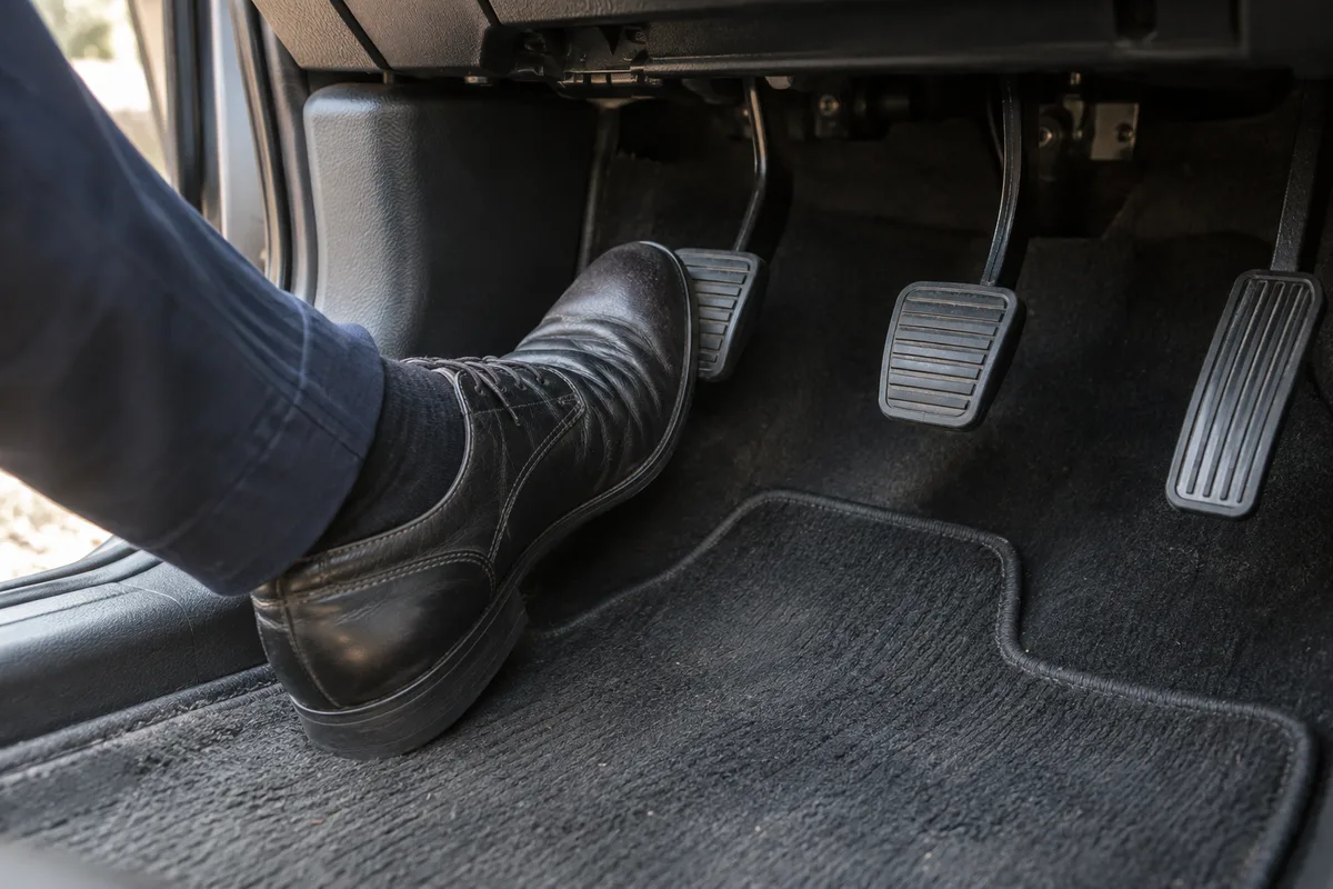 Pédalier de voiture vu de côté avec une chaussure posée sur la pédale d’embrayage